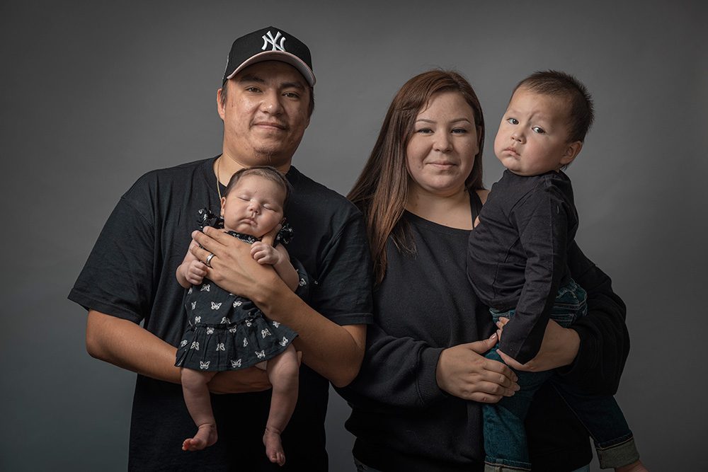 Family of four in matching black outfits with newborn and toddler studio portrait