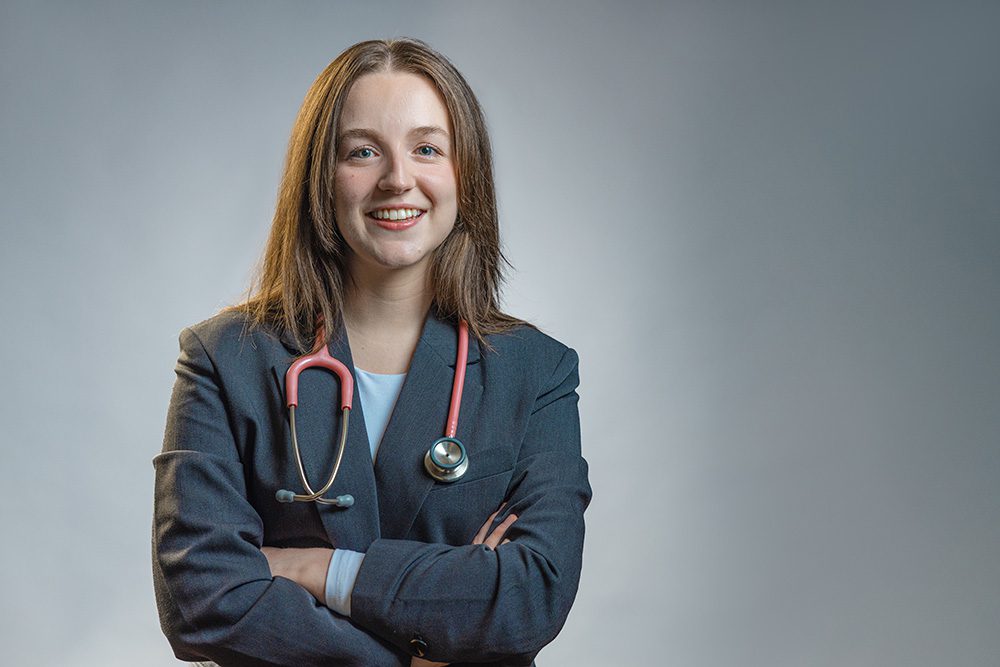 Medical student with arms crossed wearing stethoscope professional portrait gray background