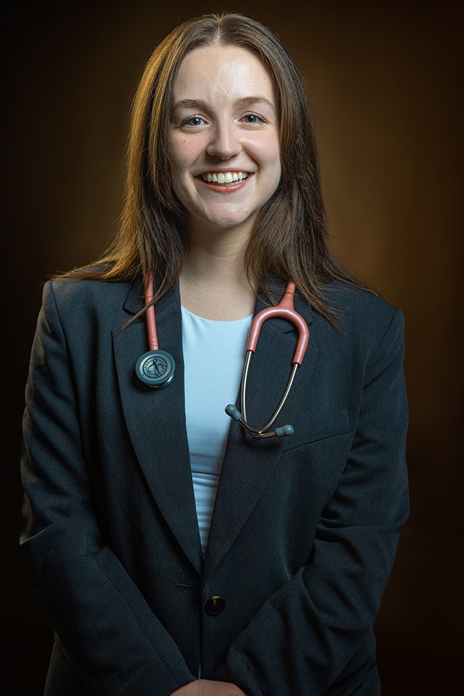 Professional headshot of medical student in navy blazer with pink stethoscope on warm background