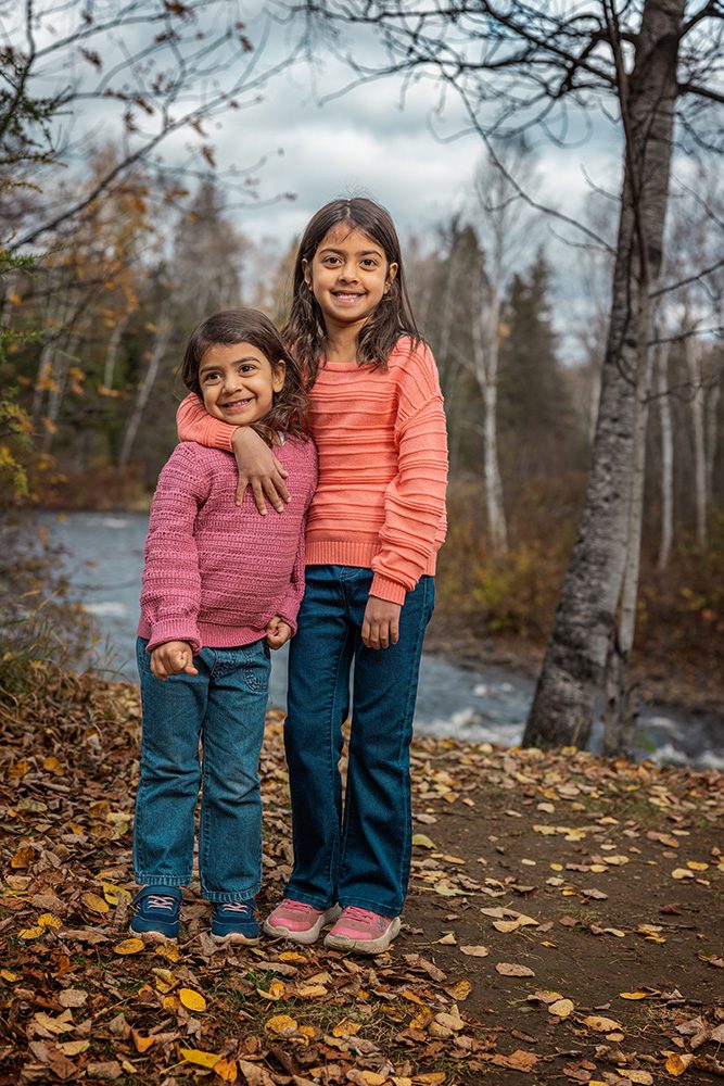 Two sisters in pink and coral sweaters standing by river autumn background