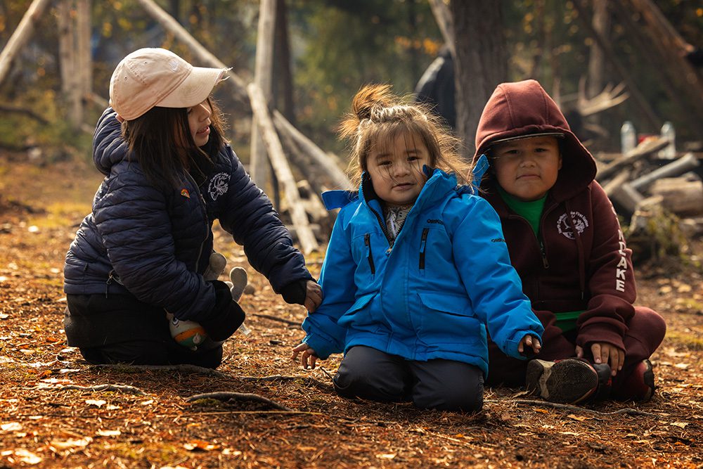 Children sitting together on the forest ground during the Moose Festival at North Caribou Lake