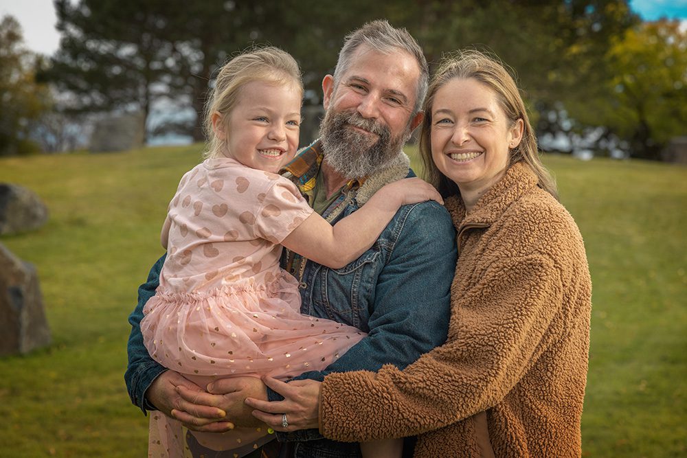 Close-up of family embracing with daughter arms around parents during outdoor portrait