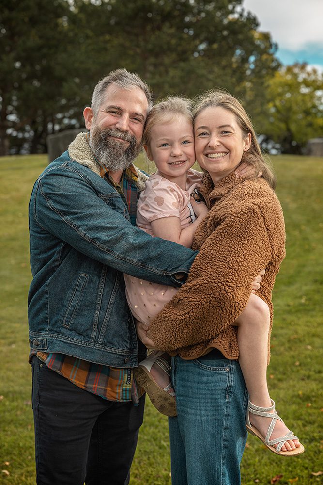 Family group hug with parents holding daughter during autumn park photoshoot