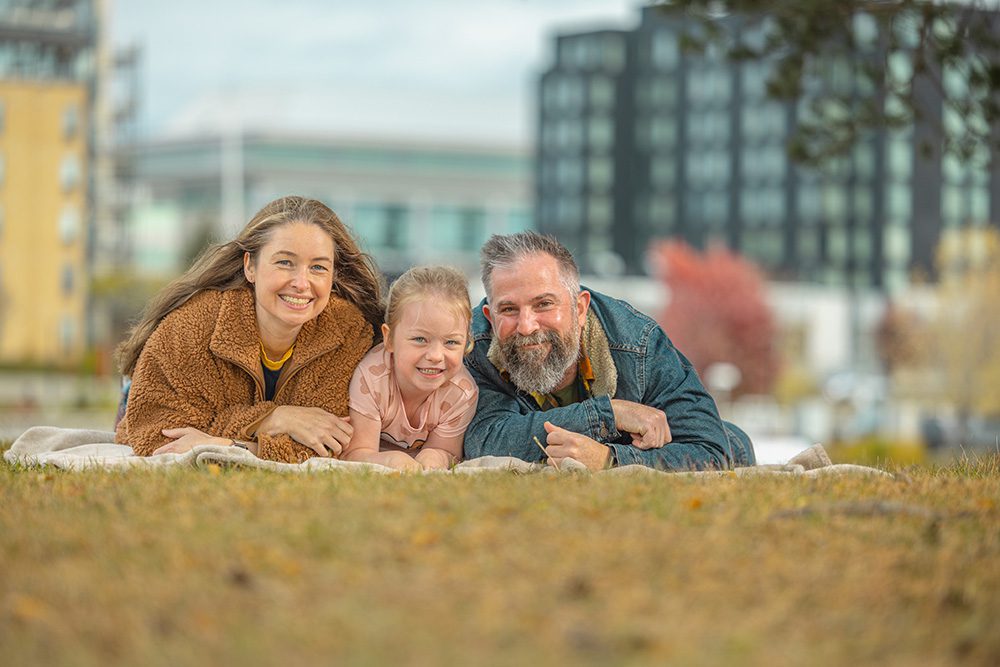 Mother father and daughter laying on blanket pointing toward camera in playful family portrait
