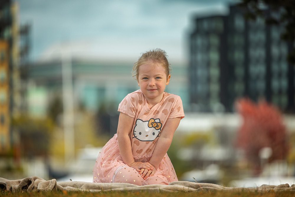 Young girl in pink Hello Kitty dress smiling at camera during outdoor portrait session
