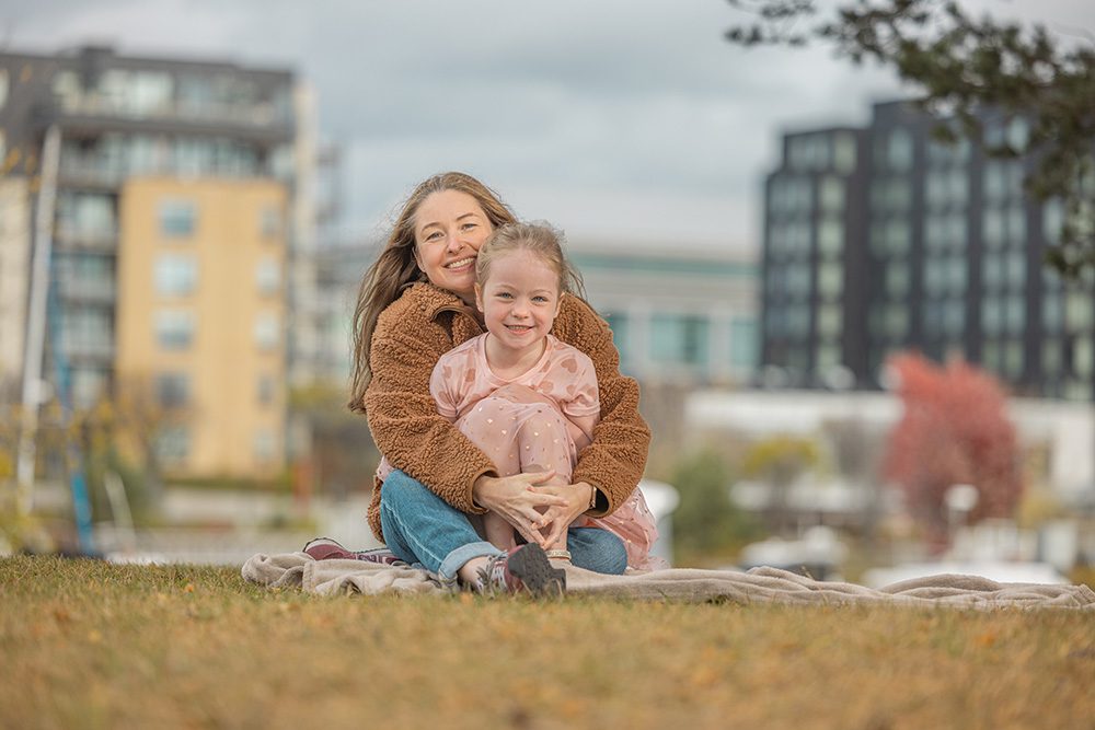 Mother and daughter sitting together on blanket with urban waterfront background