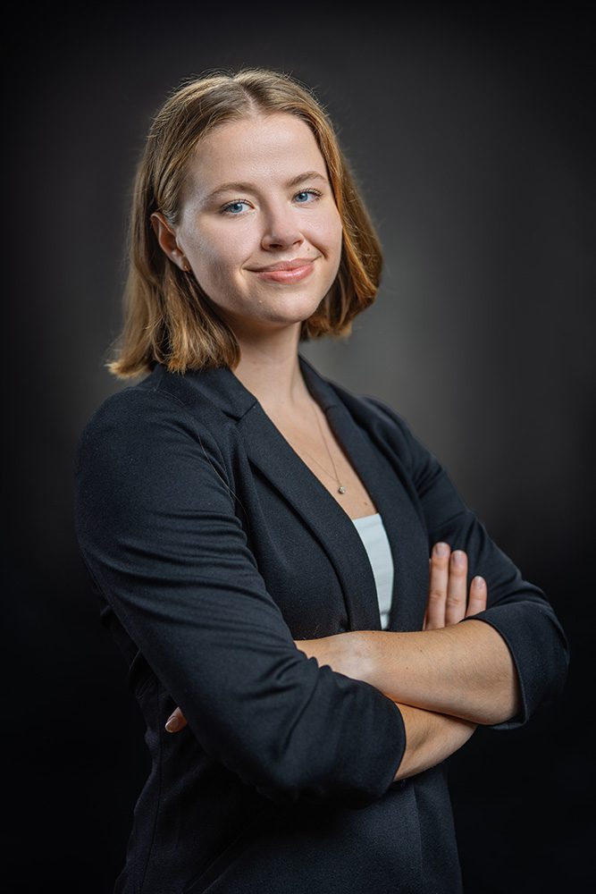 Professional business headshot young woman black blazer arms crossed dark background