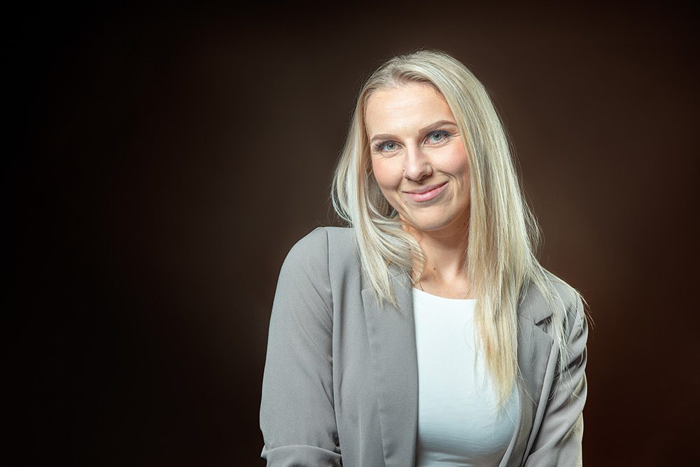 Business headshot blonde woman gray blazer warm background professional photo