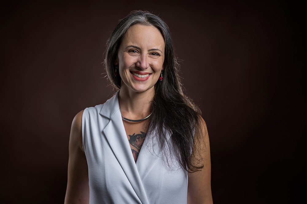 Professional woman in light blue vest smiling warmly against brown studio background