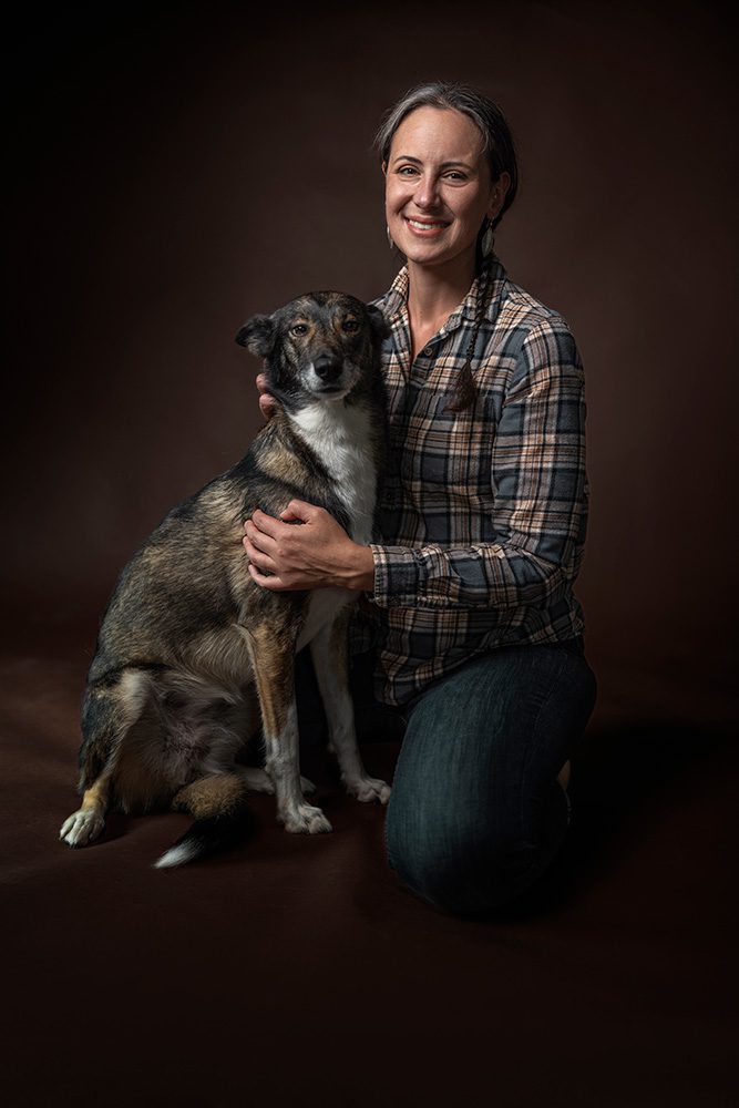 Professional Pet Portraits Thunder Bay of woman kneeling with dog both looking at camera on brown background