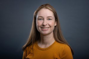 Young professional woman in mustard yellow sweater against gray studio background headshot