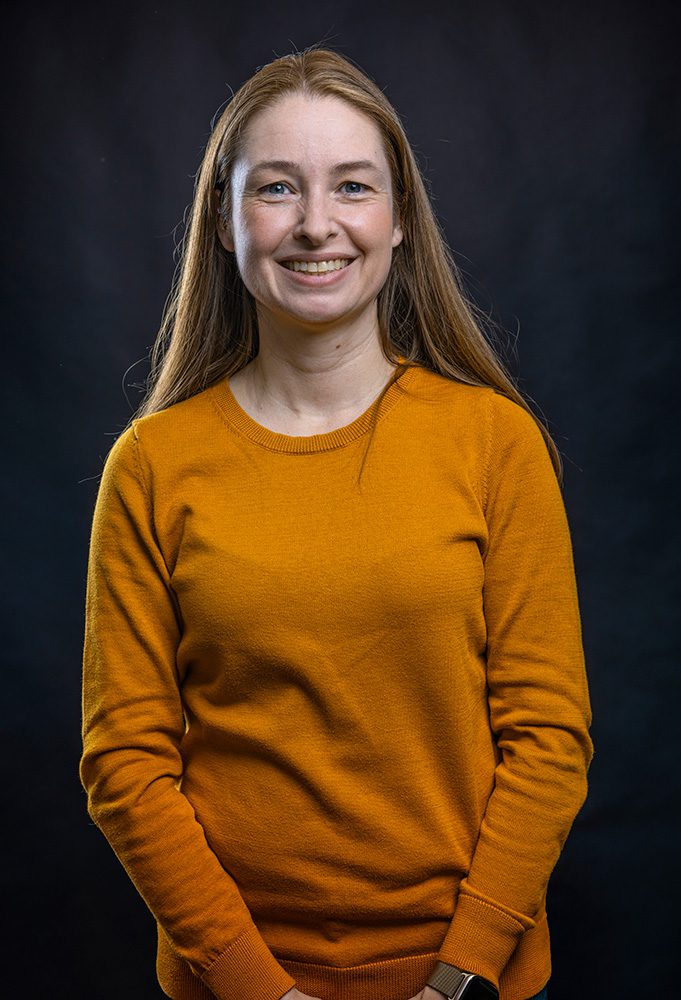Professional portrait of woman in yellow sweater against black background with hands in pockets