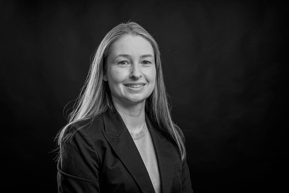 Black and white professional headshot of woman in dark blazer turned to side