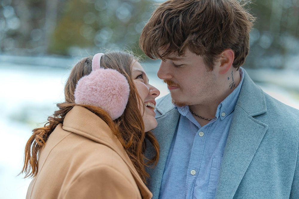 A close-up of a couple smiling at each other outdoors in winter.