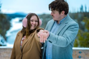 A couple holds out a hand to show an engagement ring with Kakabeka Falls in the background.