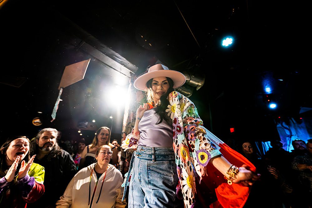 Model in pink hat and floral kimono walking runway with dramatic lighting