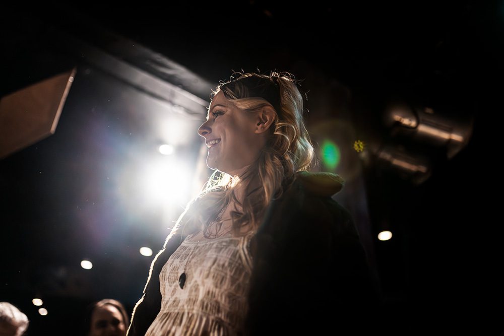 Model in white dress with flower crown backlit on runway