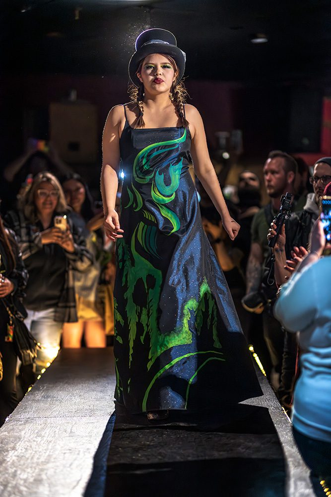 Model in swirling blue and green painted dress with top hat on runway