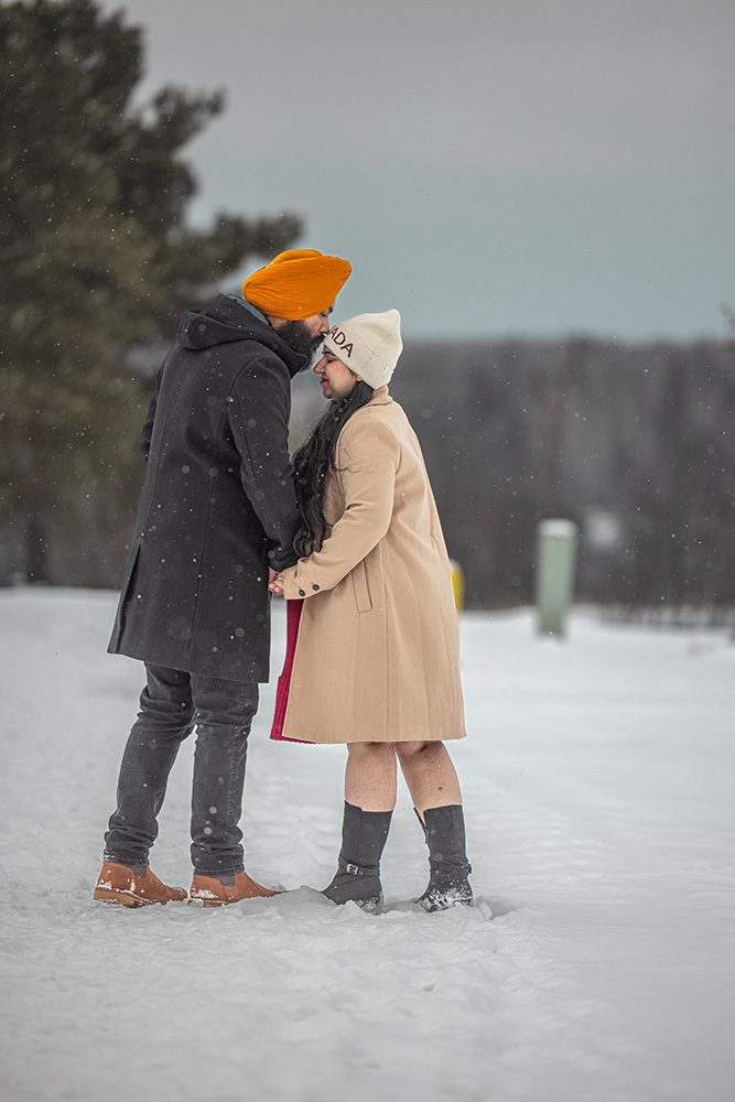 Tender forehead kiss during winter maternity photoshoot in snowy landscape