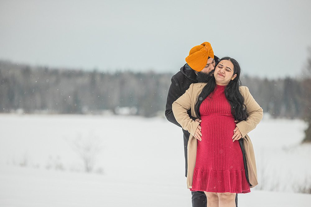 Partner kissing pregnant woman during romantic winter maternity photoshoot session