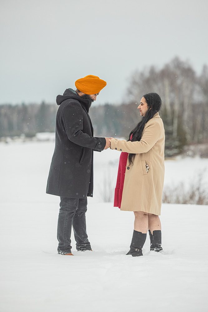 Expecting couple holding hands during winter maternity photoshoot in falling snow