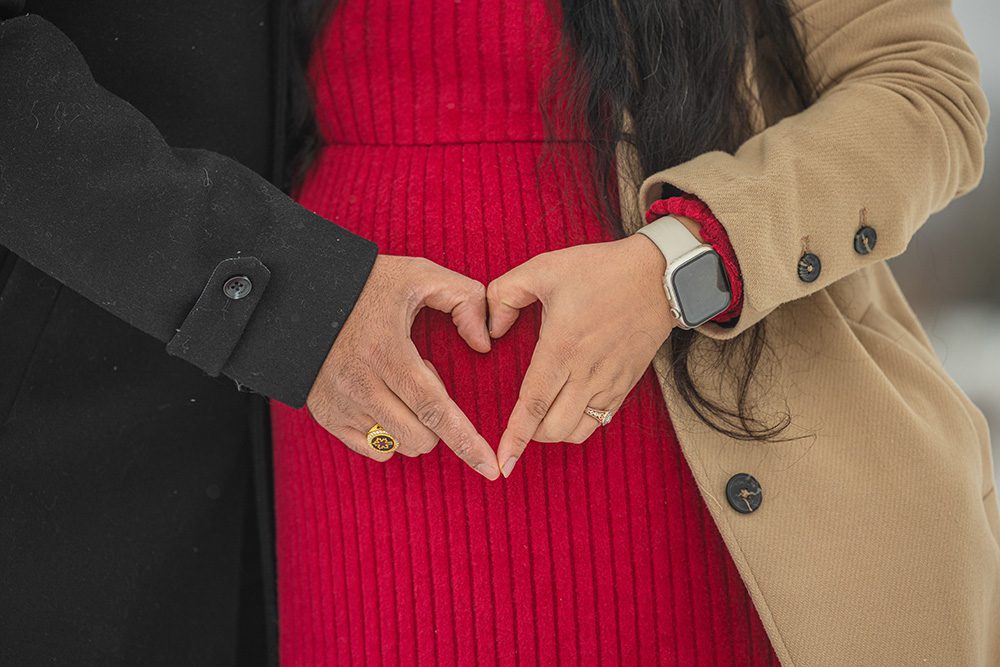 Expectant parents making heart shape with hands on baby bump during winter session
