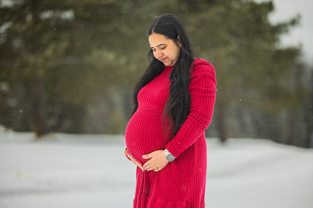 Pregnant woman cradling baby bump in red dress during winter maternity session