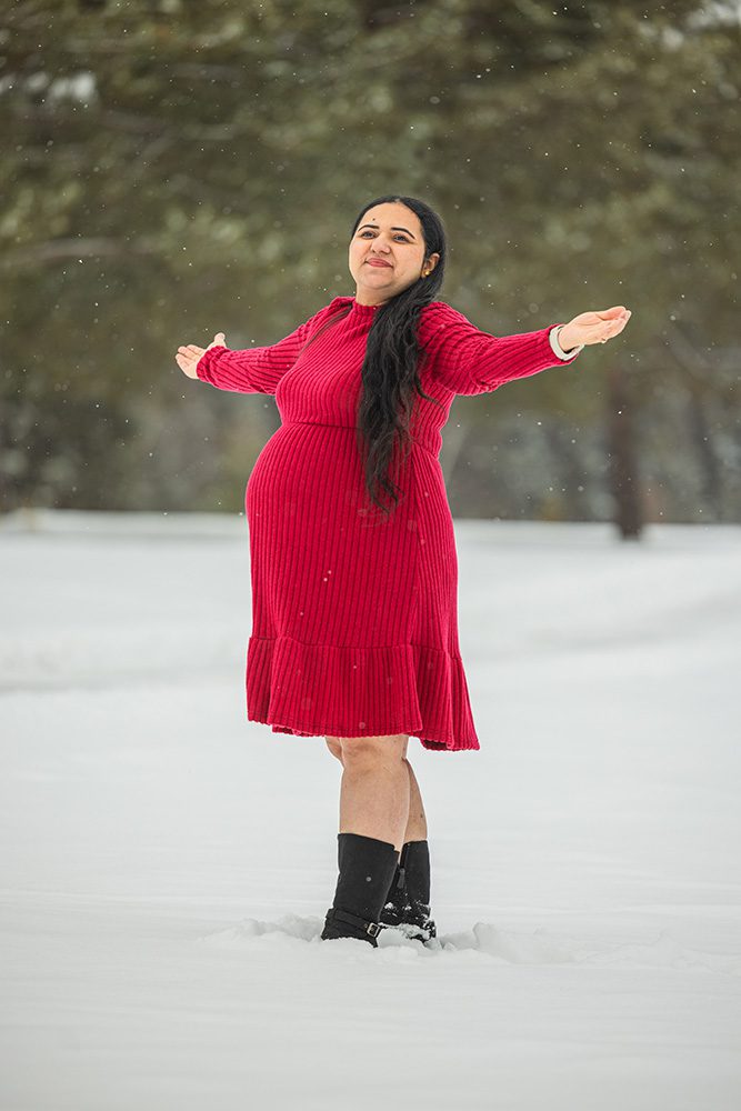 Joyful pregnant woman with arms spread wide during winter maternity photoshoot in snow