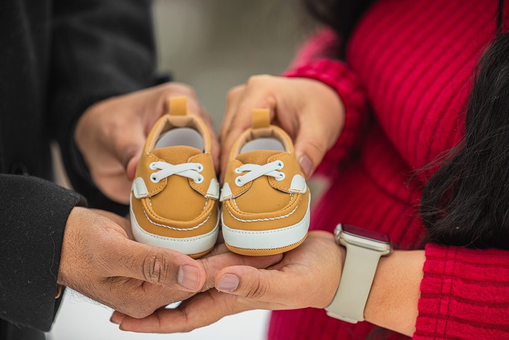Close-up of expectant parents hands holding baby shoes during winter maternity photoshoot