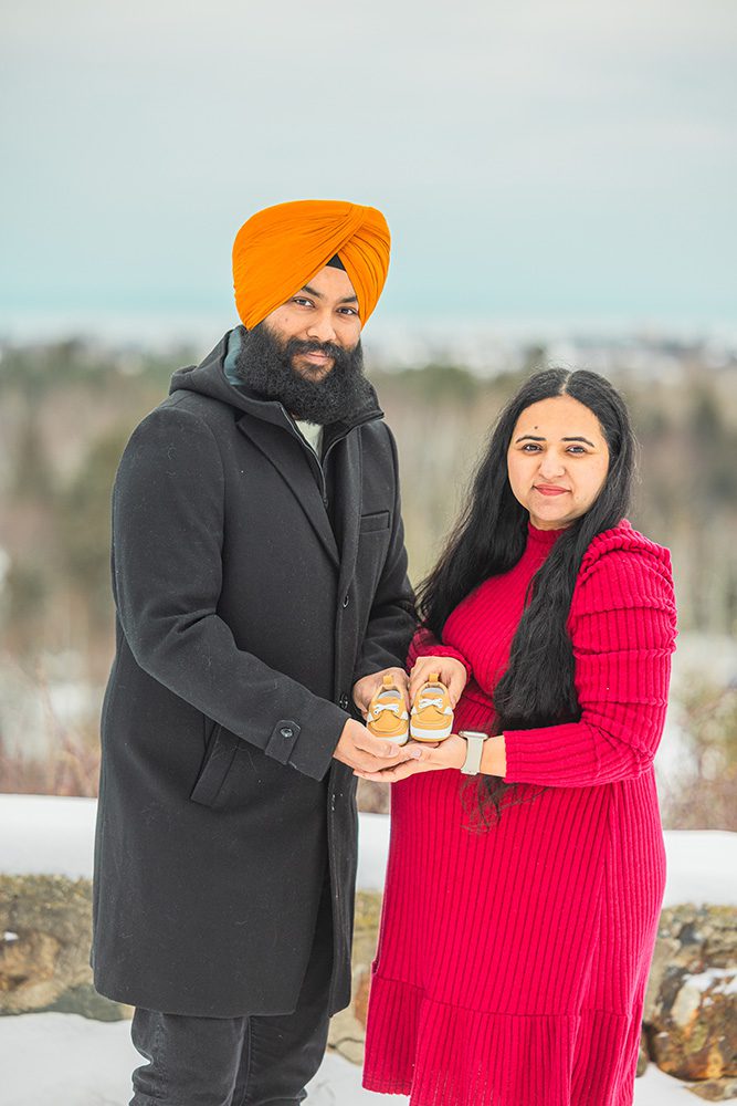 Expecting parents holding tiny baby shoes together during winter maternity session in snow