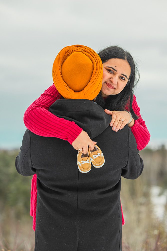 Expecting couple embracing outdoors during winter maternity photoshoot with baby shoes prop