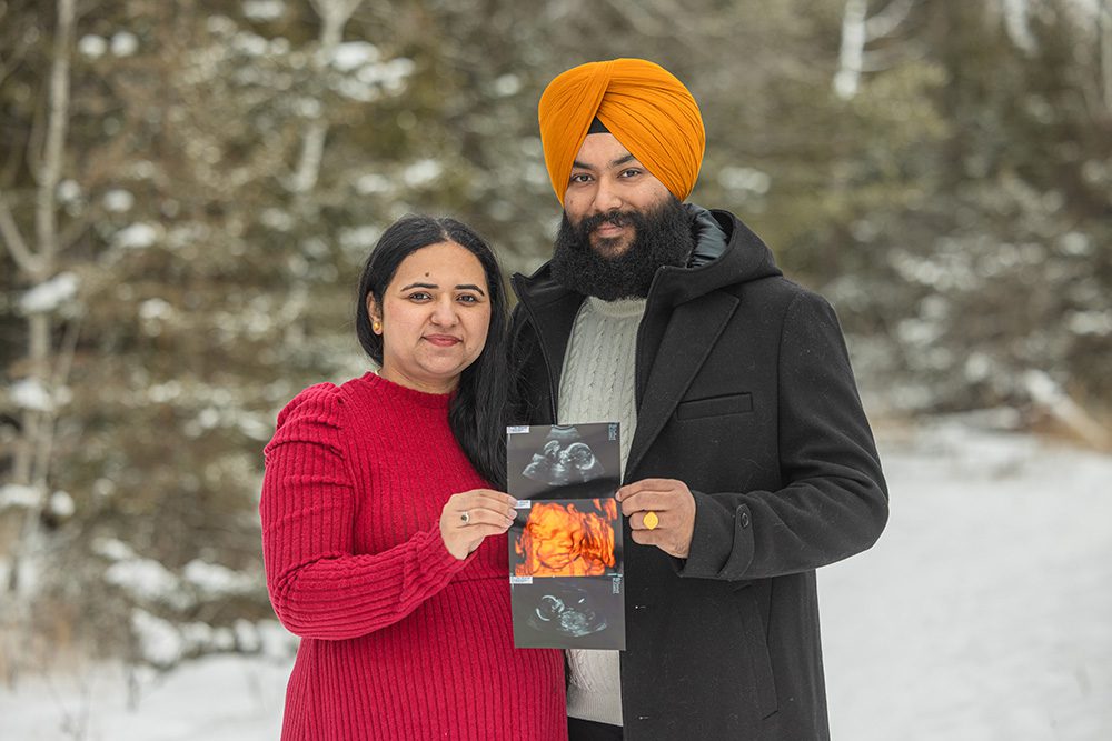 Expecting couple holding ultrasound photos during winter maternity photoshoot in snow