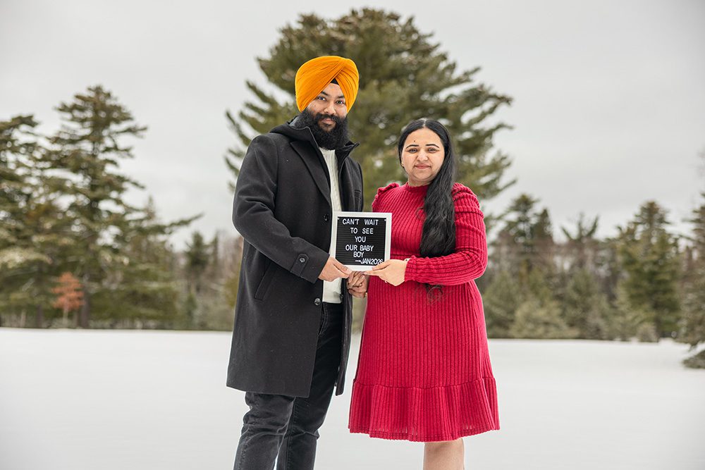 Expecting couple holding baby announcement sign together during winter maternity session in snow