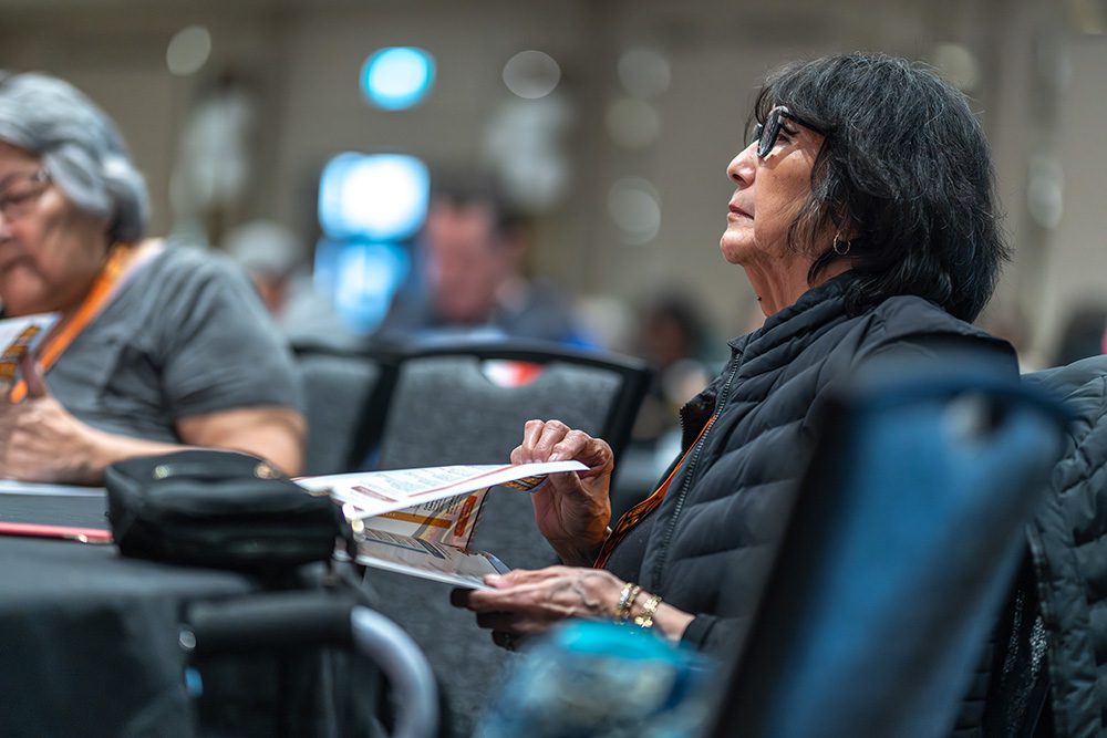 Indigenous woman listening intently at conference holding program materials