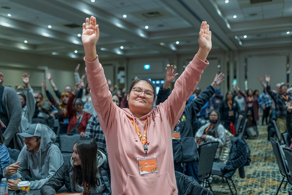 Young woman in pink hoodie celebrating with arms raised at conference