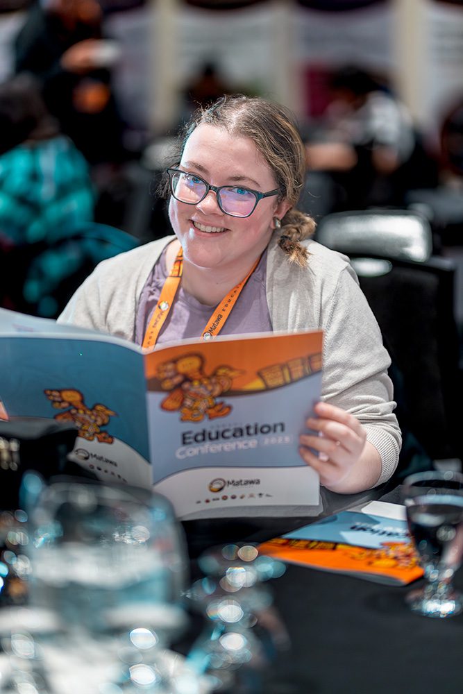 Woman in cardigan smiling while reading colorful conference education materials