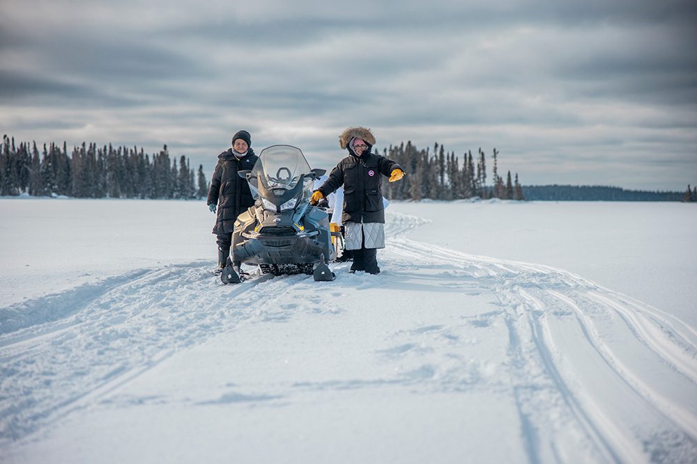 Students traveling by snowmobile across frozen lake winter camping expedition