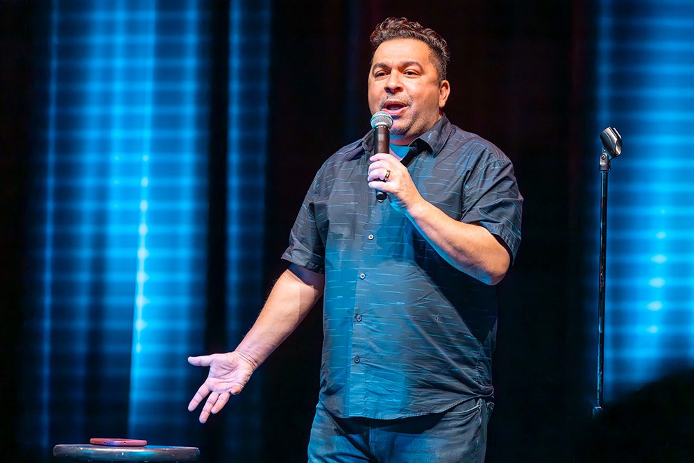 Comedian in dark shirt performing close-up shot under blue stage lights