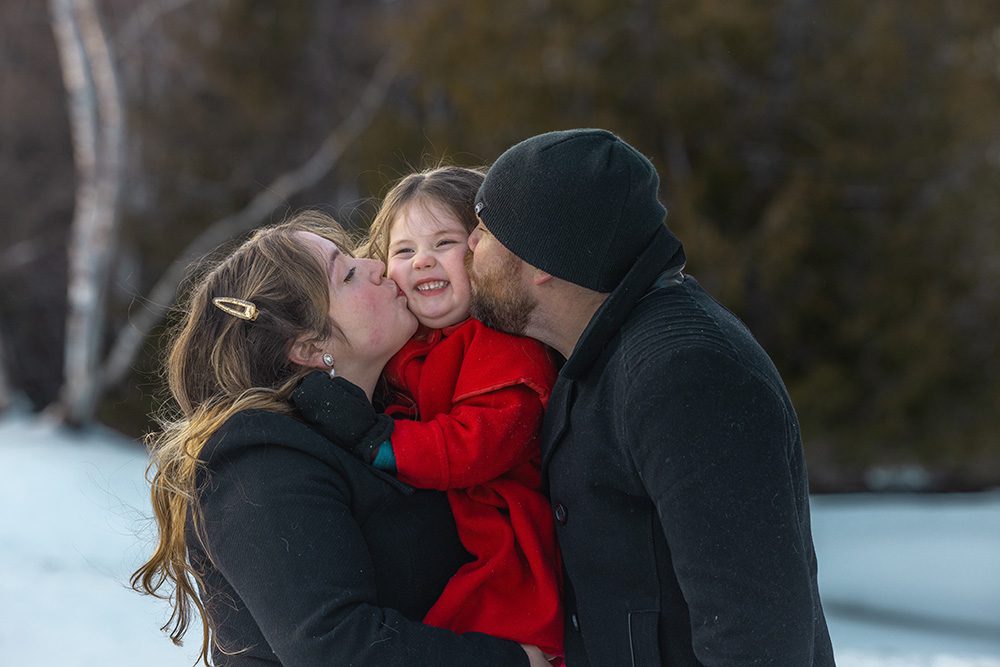 Parents kissing daughter simultaneously during sweet winter family photography moment