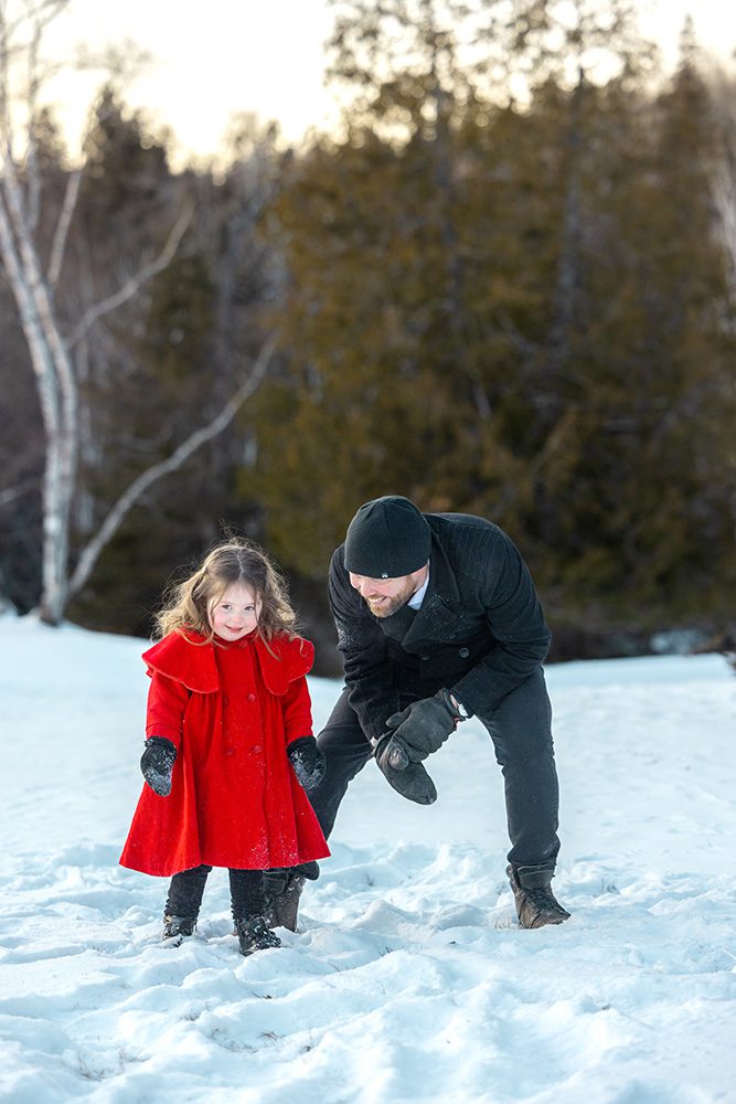 Father playfully swinging daughter in snow during energetic winter family photography