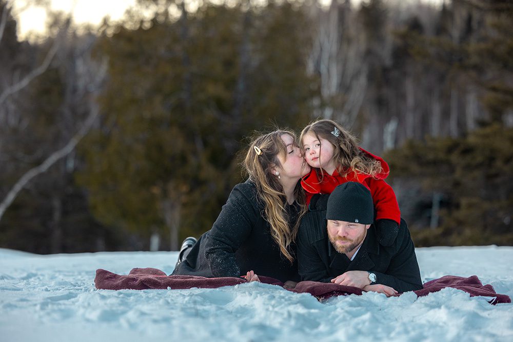 Family cuddling on blanket in snow during cozy winter photography session
