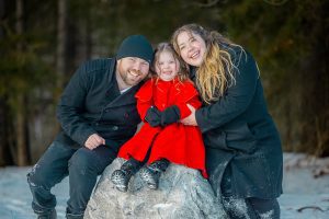 Happy family sitting together on rock during playful winter family photography session