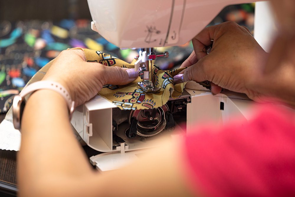 Close-up of hands sewing colorful Indigenous-patterned fabric on sewing machine