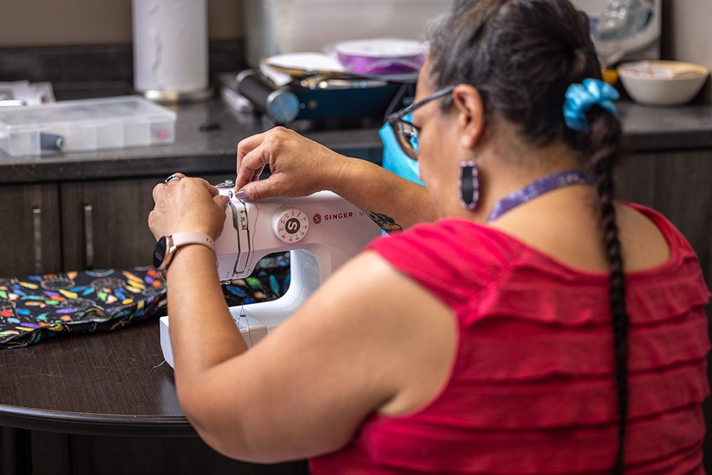 Woman in red sewing at pink Singer sewing machine during craft workshop at Anishnawbe Mushkiki