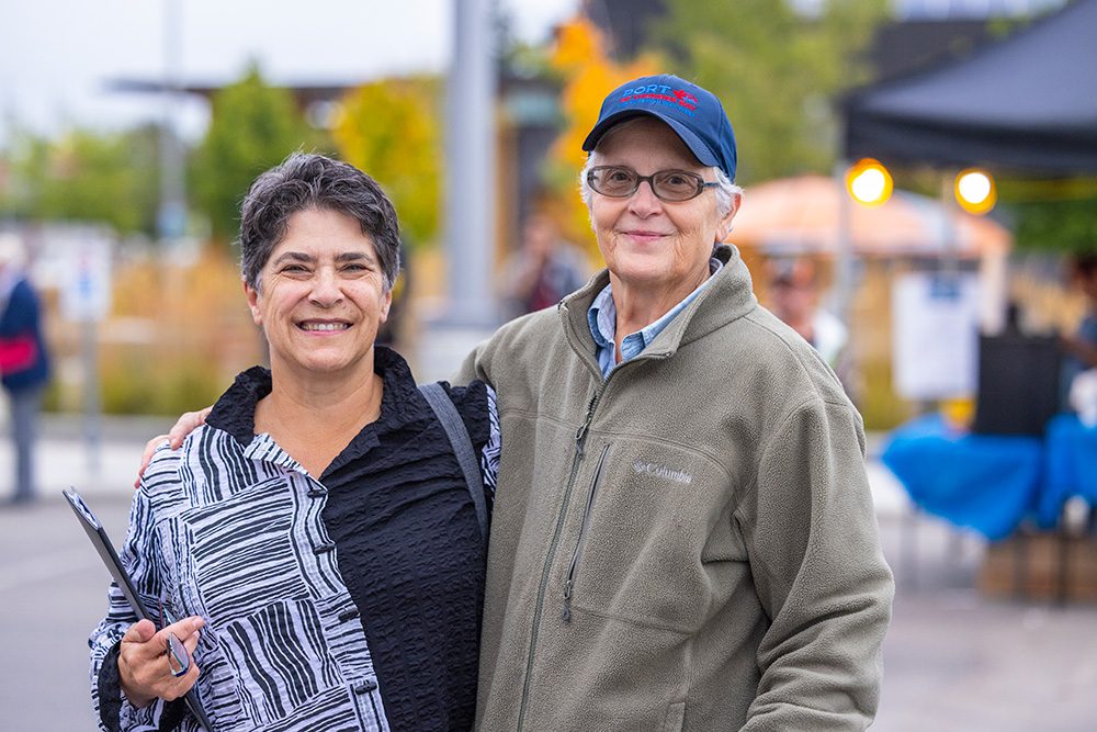 Two smiling women standing together at outdoor festival during daytime