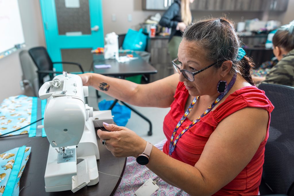 Woman in red adjusting white sewing machine during community craft program