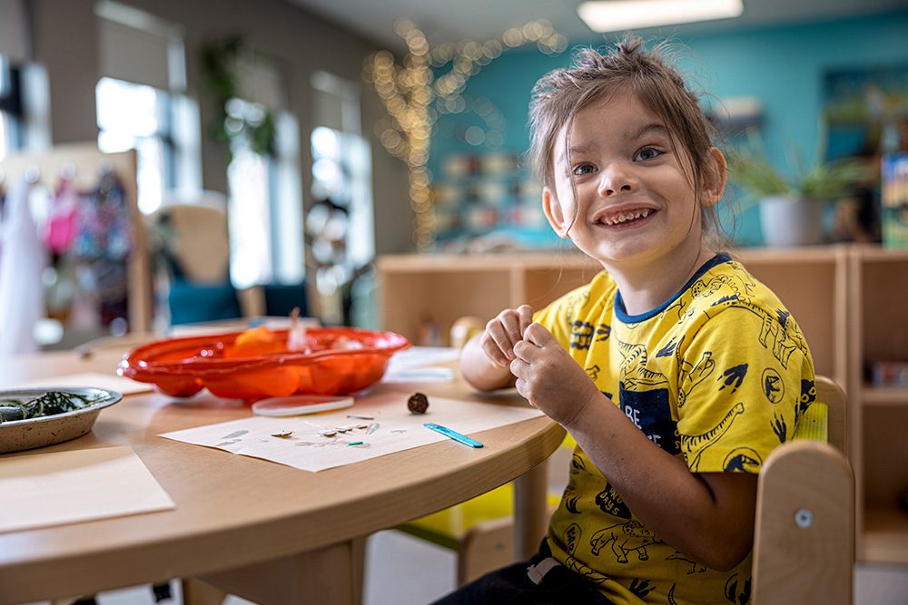 Smiling young girl in yellow shirt showing her completed craft project