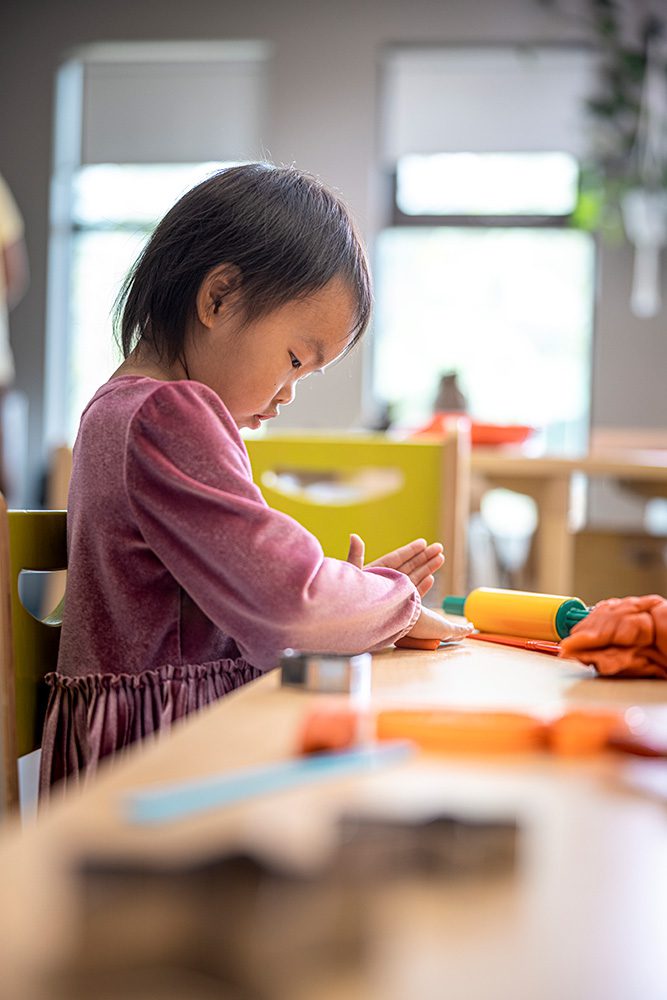 Young girl in pink concentrating on craft activity at bright community center