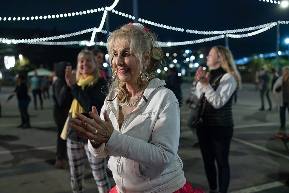 Woman in white jacket and red skirt clapping at night event