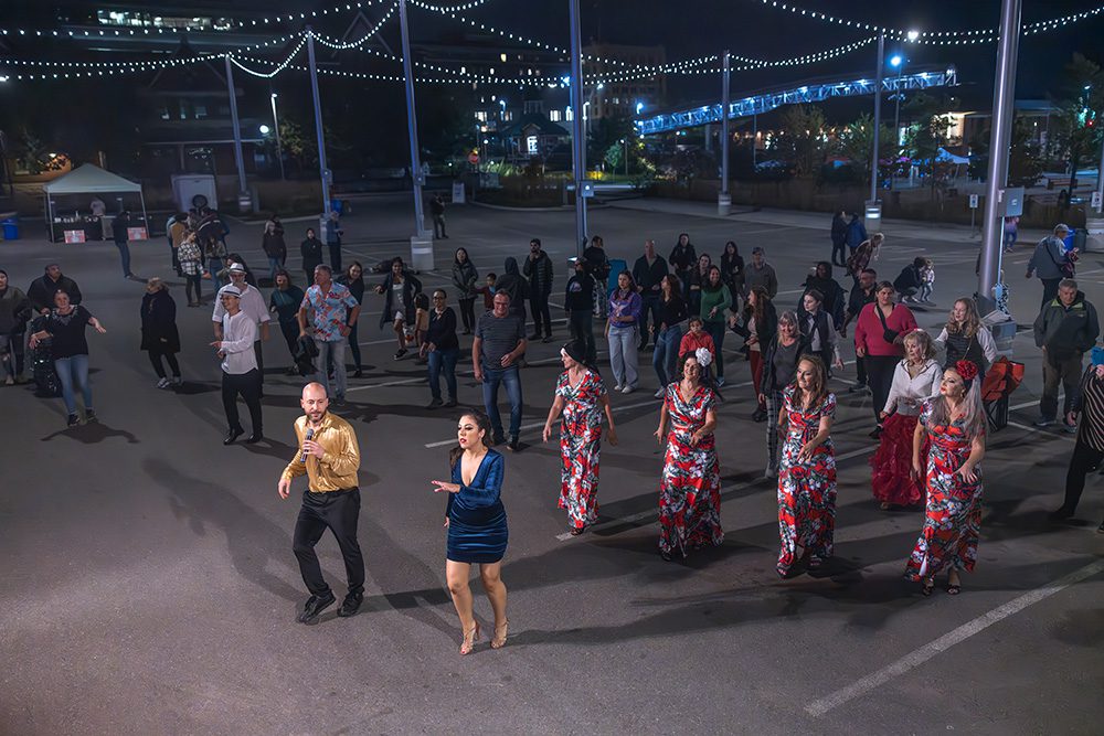 Dancers performing in street at night with crowd watching under string lights